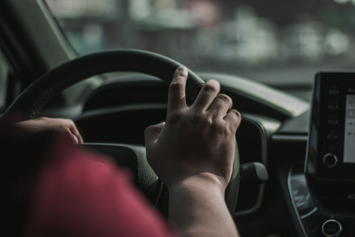 Een hand aan het stuur van een wagen, met een scherm op het dashboard
